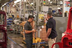 Two engineers wearing safety goggles use machinery at a manufacturing plant.