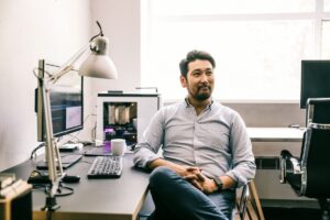 A portrait of programmer sitting at desk in an office.