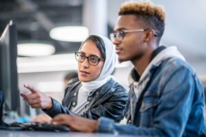 A young female student helps a classmate with a project in the computer lab.