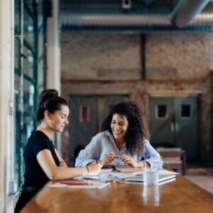 Two businesswomen talking at a conference table in a loft office.