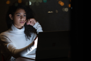 Commercial contextual lifestyle image of adult female working on Surface Book 3 in dark office.