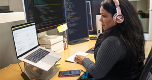 An image of a female developer coding at her desk, wearing headphones.