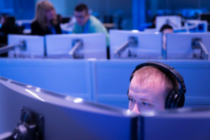 Adult male sitting behind computer screens.