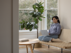 Adult female sitting on couch inside working on Surface Laptop.