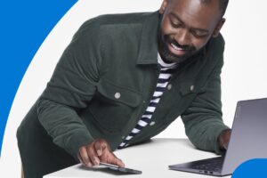 Photograph of adult male looking at Lenovo IdeaPad and mobile phone photographed in studio on white background.