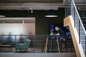 Photo of a man sitting alone at a table in an office building and works on a laptop.