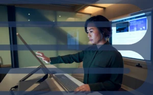 Side profile of a woman wearing a dark shirt in a dim office scrolling or working on a Microsoft Surface Studio.