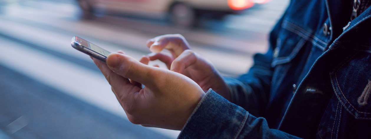 Close up of a person using their smart phone, with traffic in the background