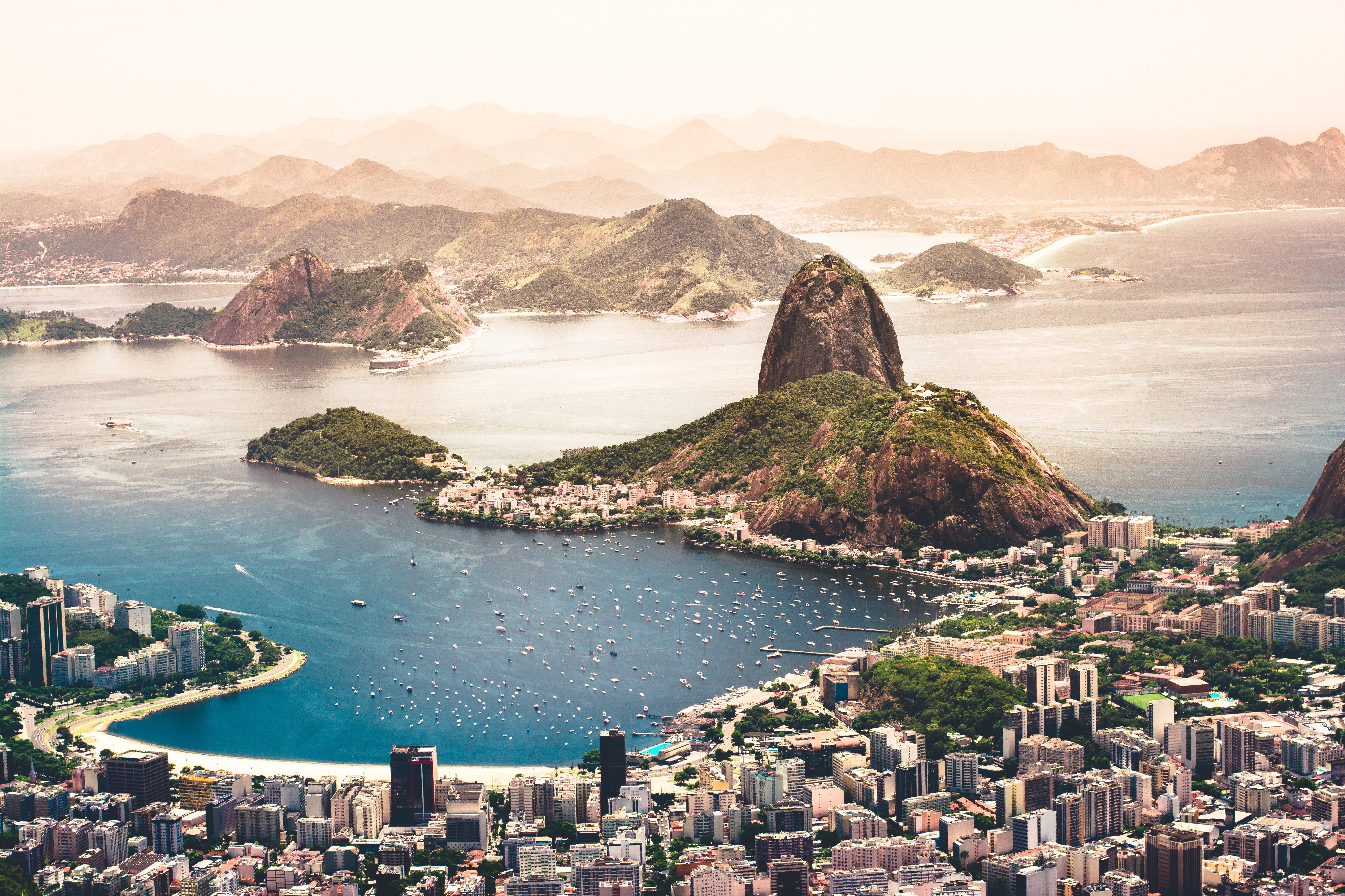 Skyscrapers and other buildings line the waters of Rio de Janeiro's warm-looking Guanabara Bay. The rocky Sugarloaf Mountain is in the background.