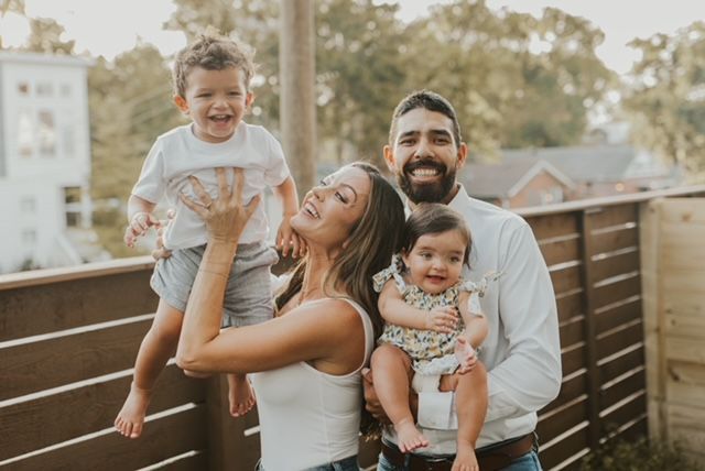 A family is posing for a picture in front of a wooden fence.