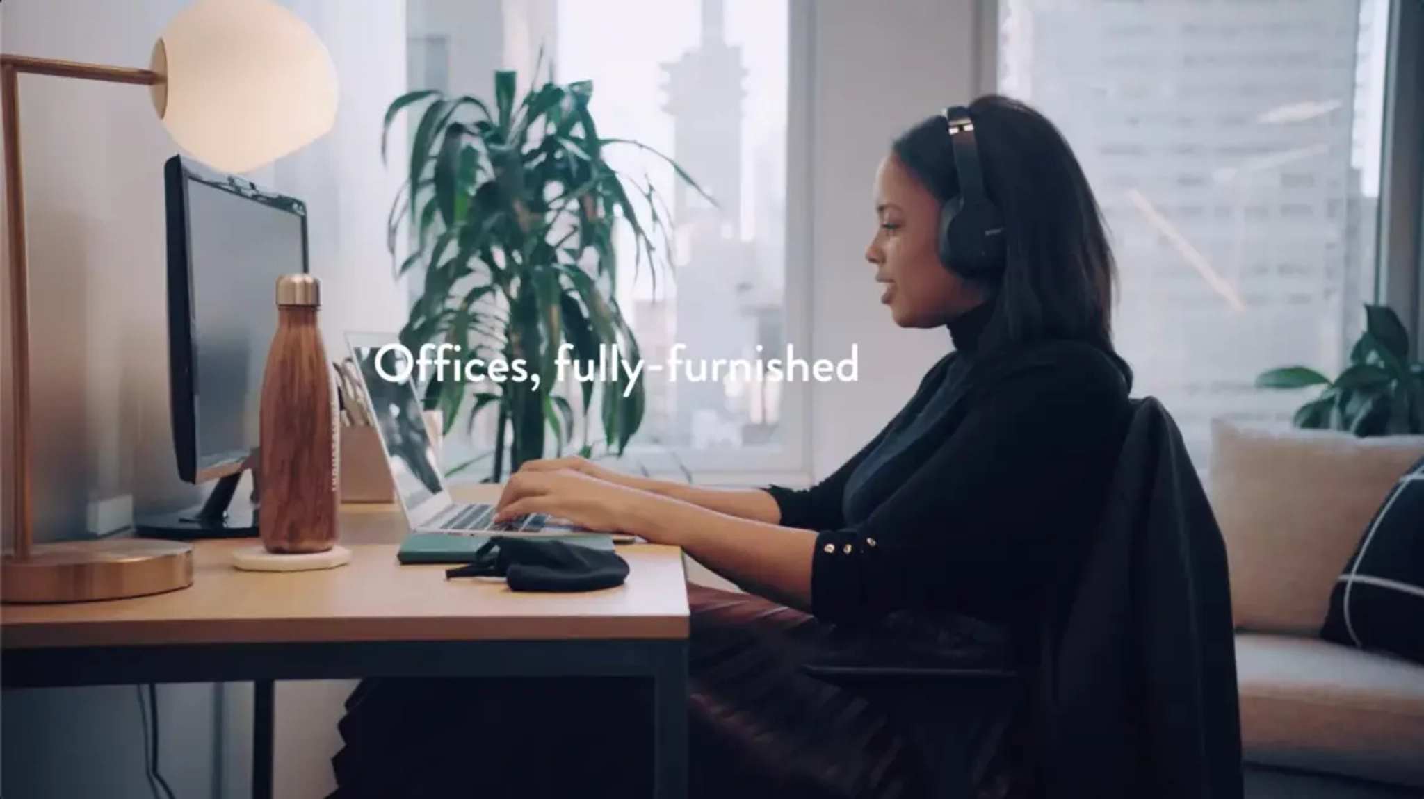 A woman at her desk with a lamp, a water bottle and a screen