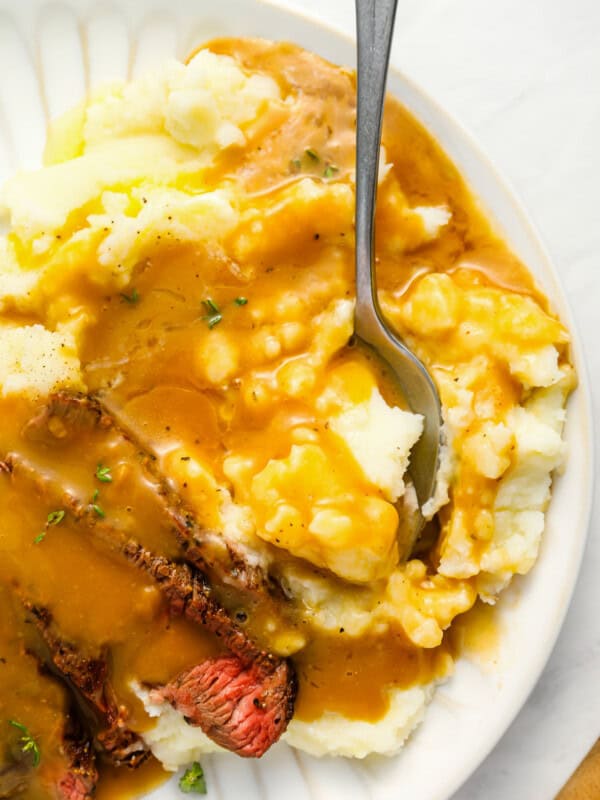 close up of brown gravy over mashed potatoes on a white plate.