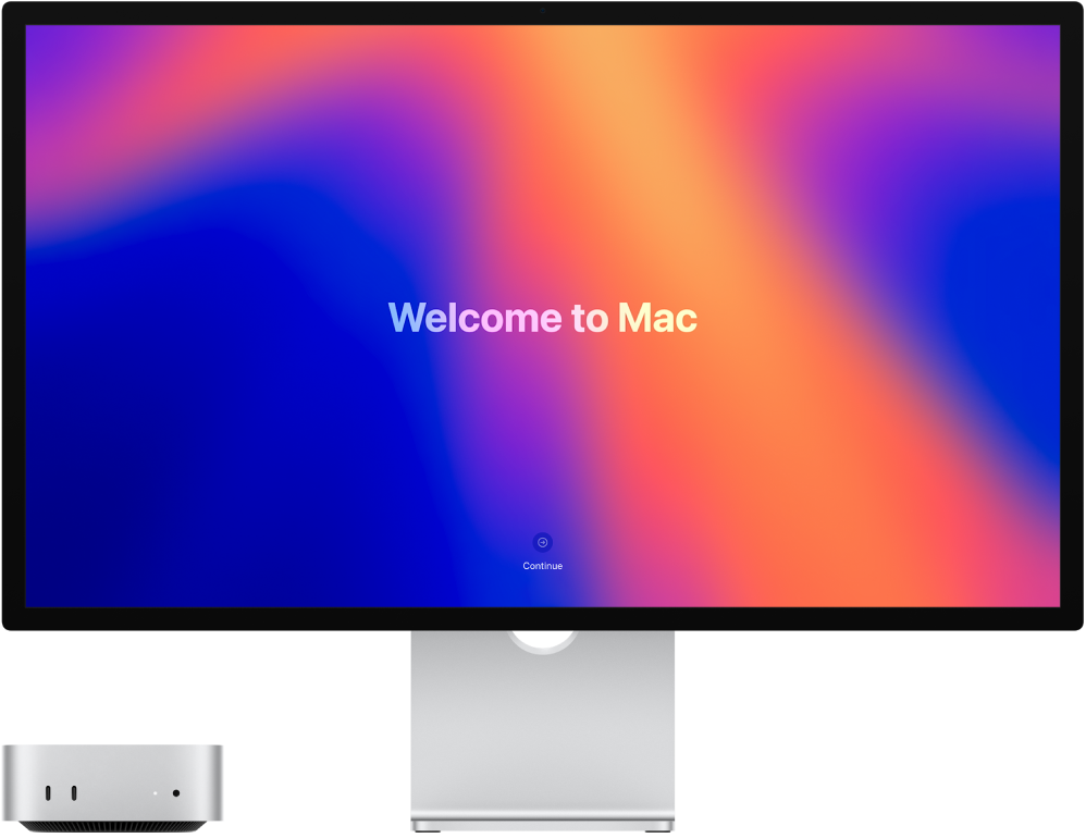 Mac mini a Studio Display vedle sebe. Na monitoru je vidět text „Vítá vás Mac“.