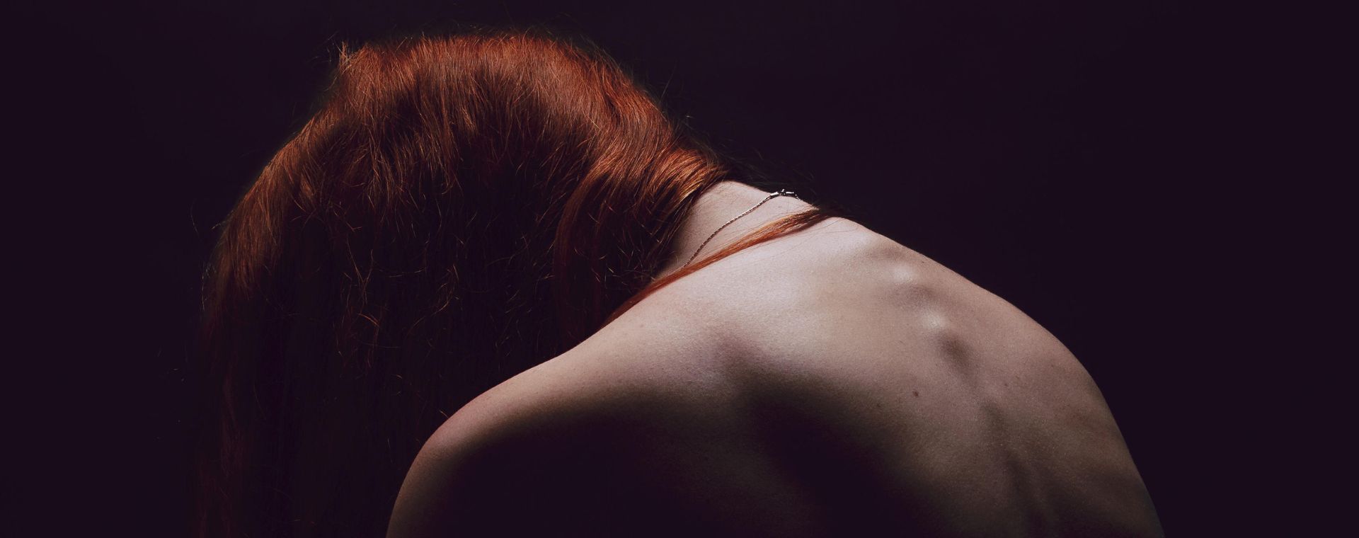 Rear view of very thin redhead woman being ashamed of her body. Underweight female feeling sad over dark background. - Image ID: RB5022 (RF)