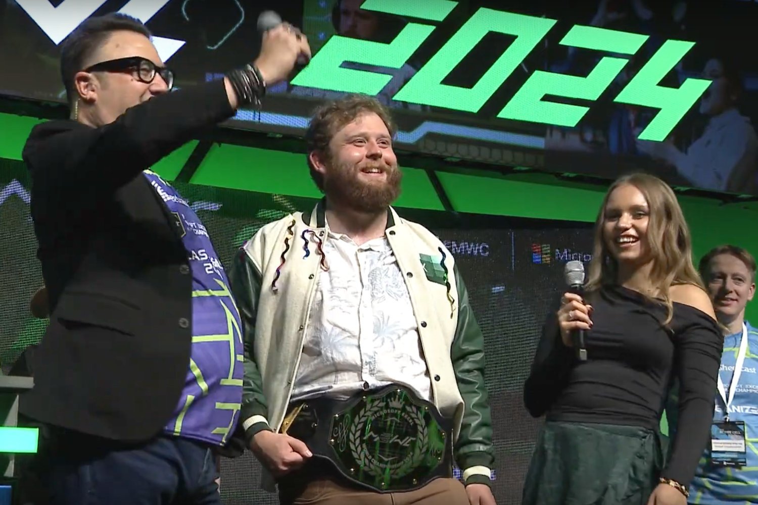 Michael Jarman, pictured between two people, on stage at the Microsoft Excel World Championships with his Championship belt.