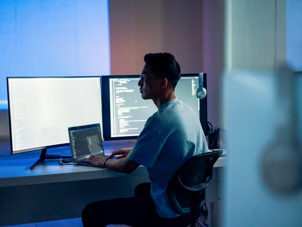 Man working at a laptop computer with two monitors attached