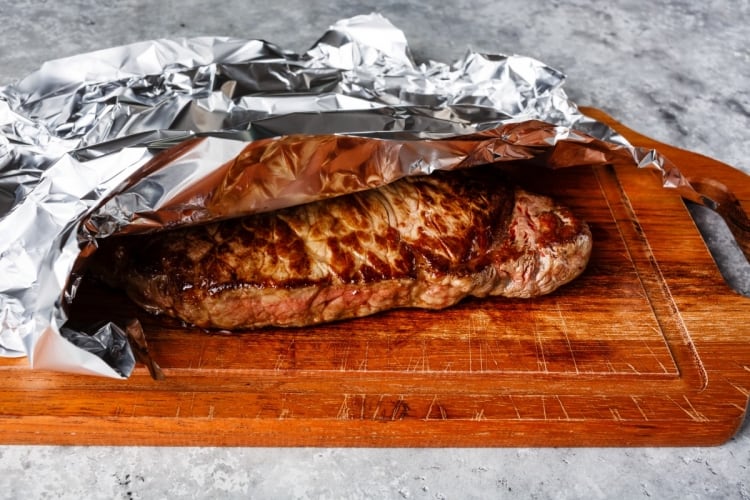 A steak resting under foil on a cutting board.