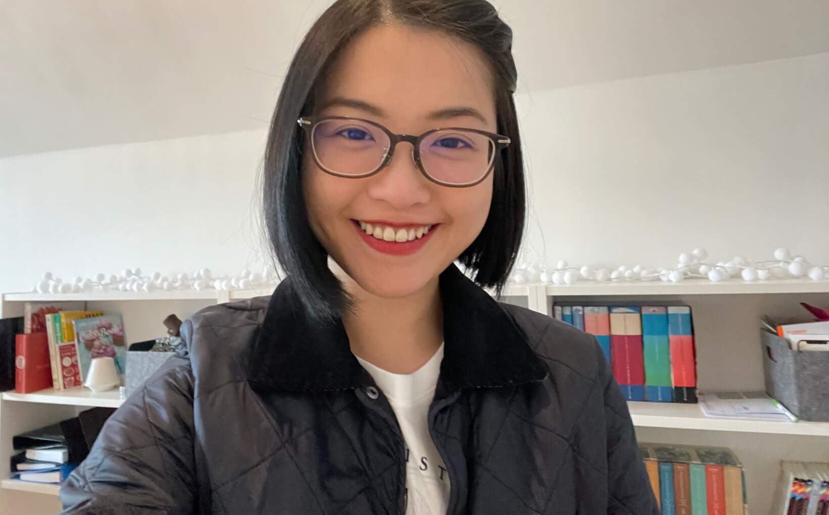 Coie smiles to the camera. She's standing in front of a bookshelf.