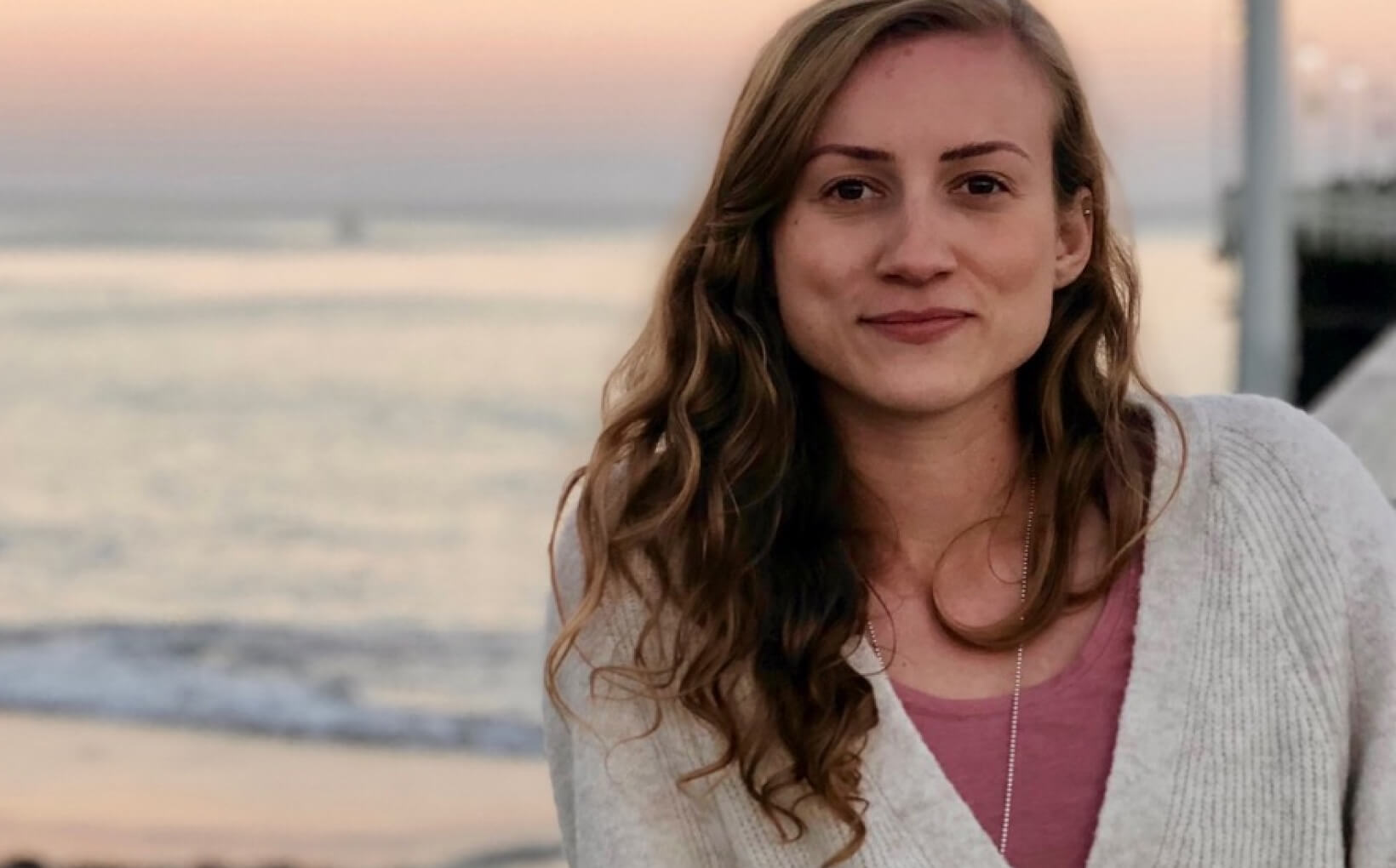 Lynn smiling to the camera with a beach in the background.