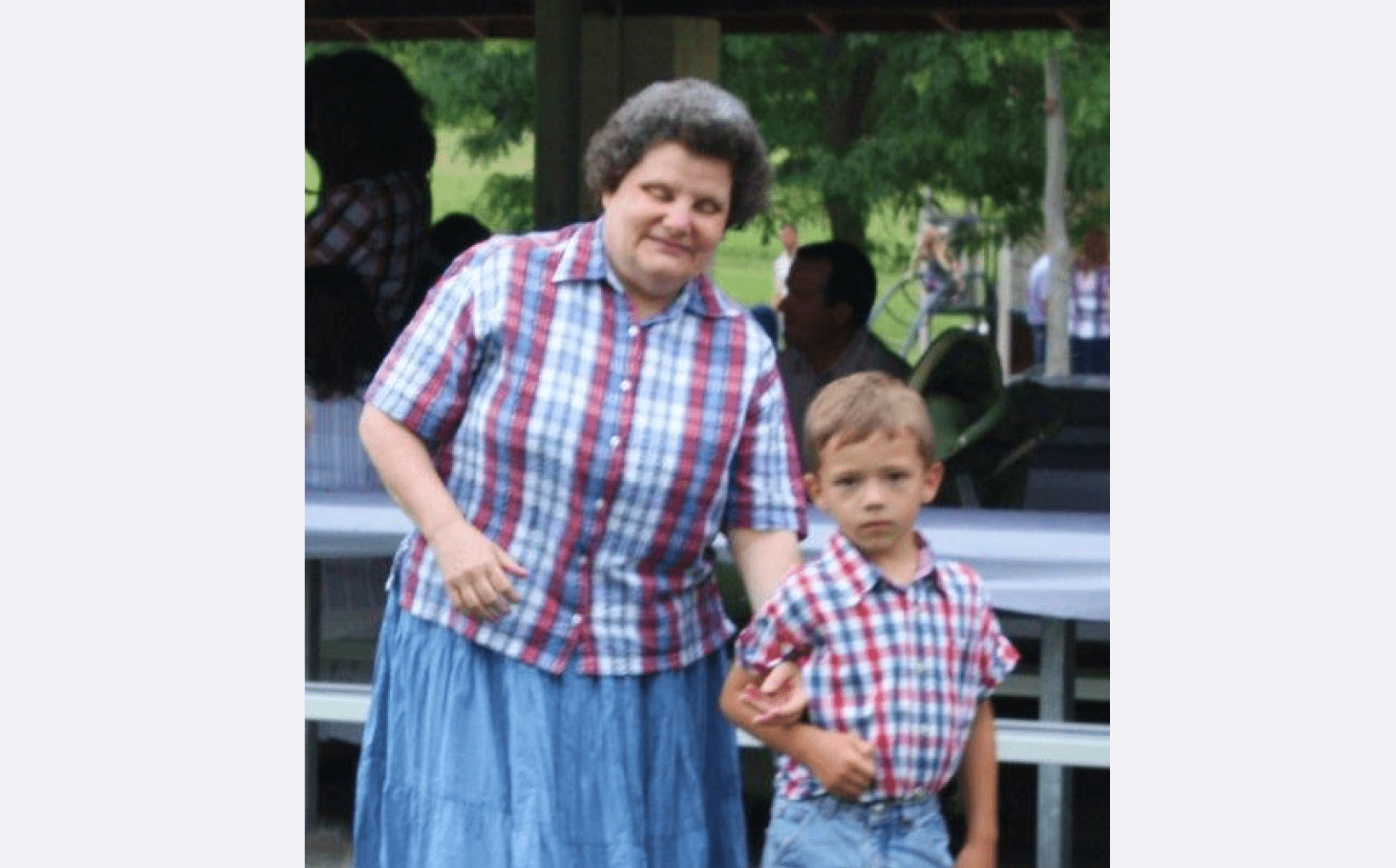 Penny standing with one of her students. They are both wearing checkered shirts and light blue bottoms.