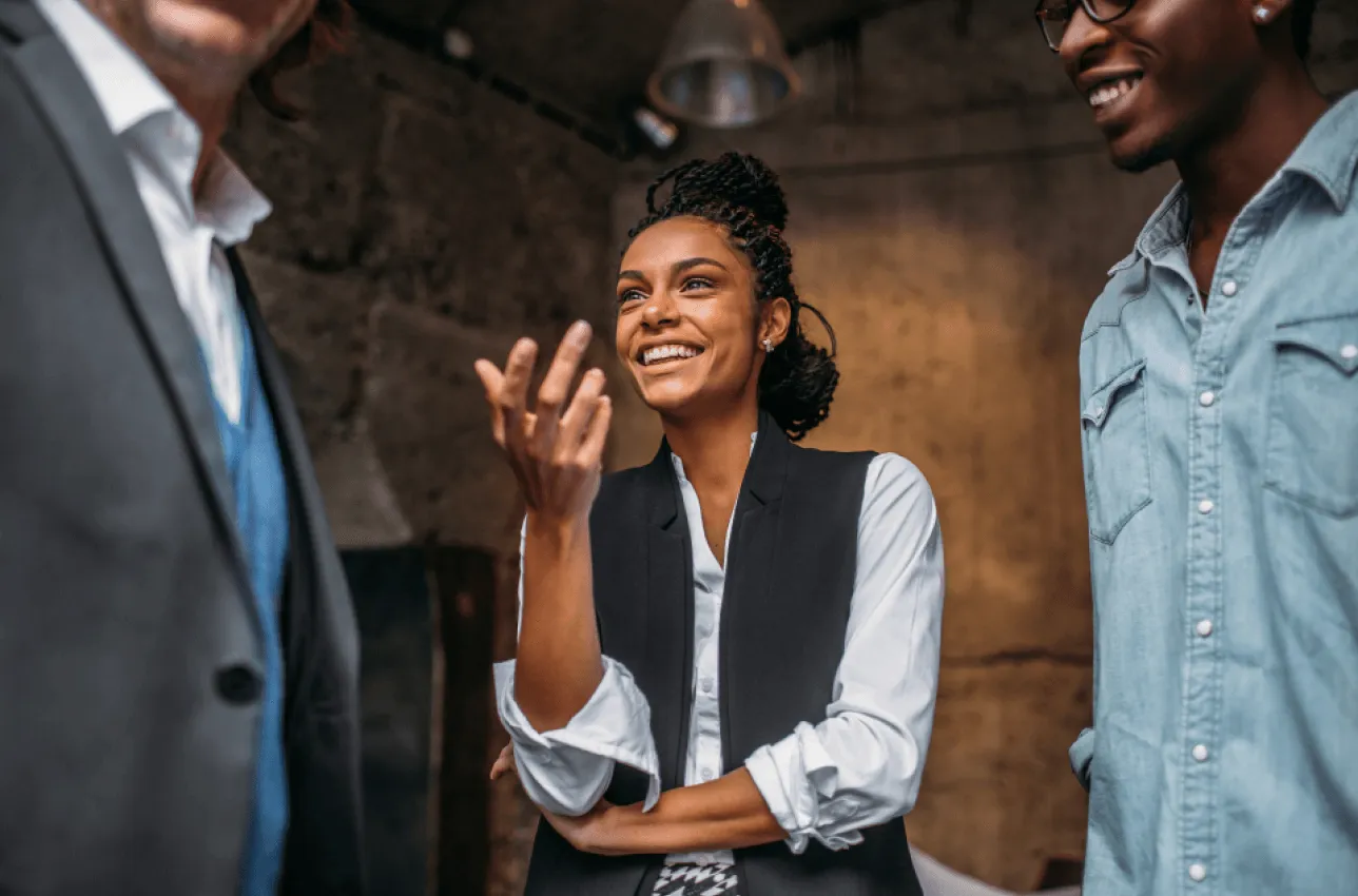 Group of three professionals standing around smiling while one gesticulates with their hand.