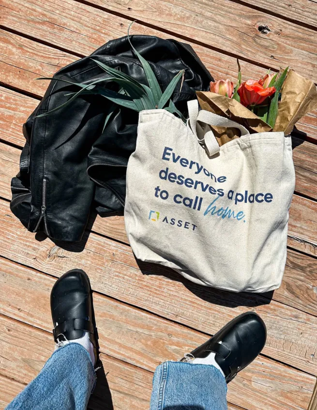 Asset tote bag on ground that says "everyone deserves a place to call home"