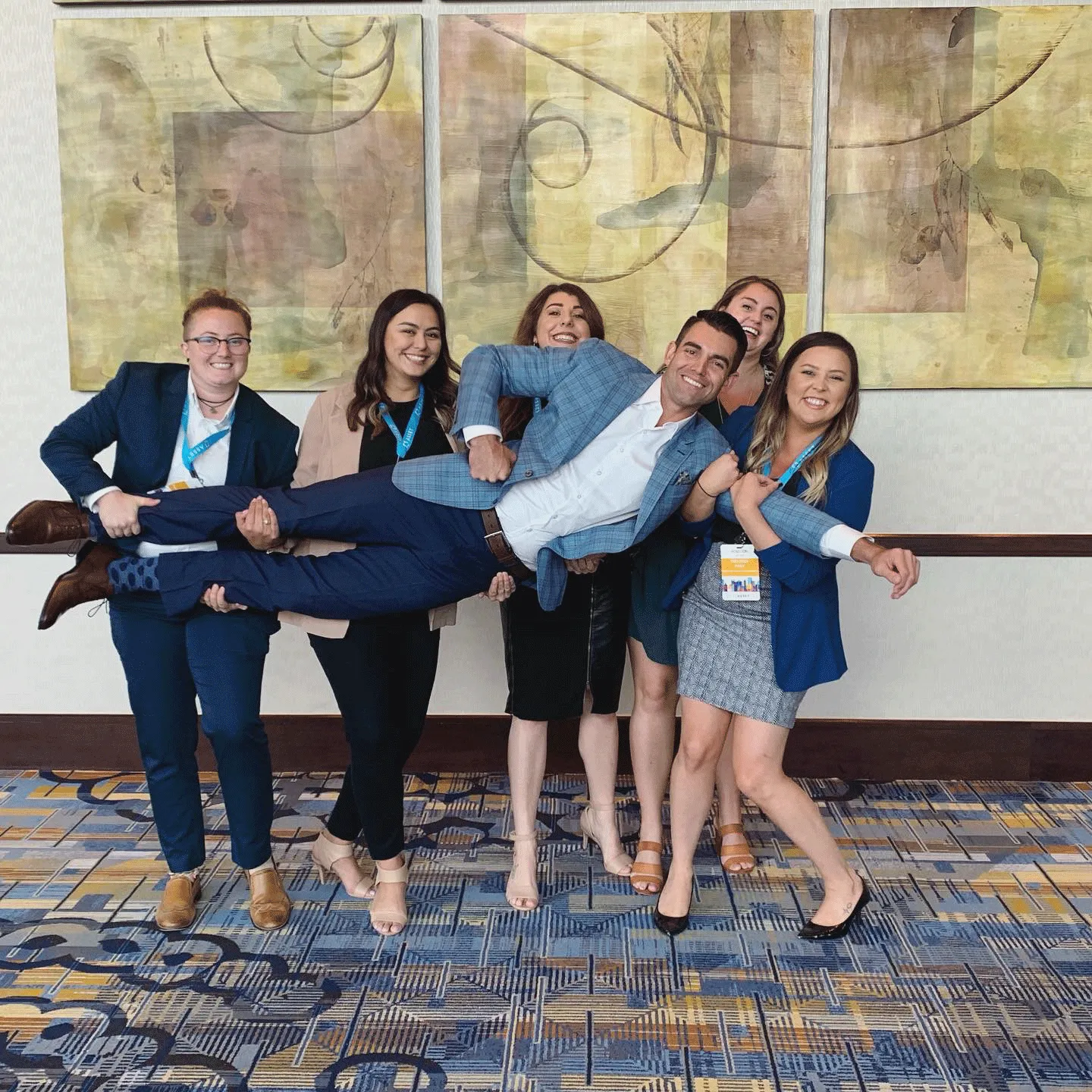 Group of Asset employees holding up another employee at a conference 