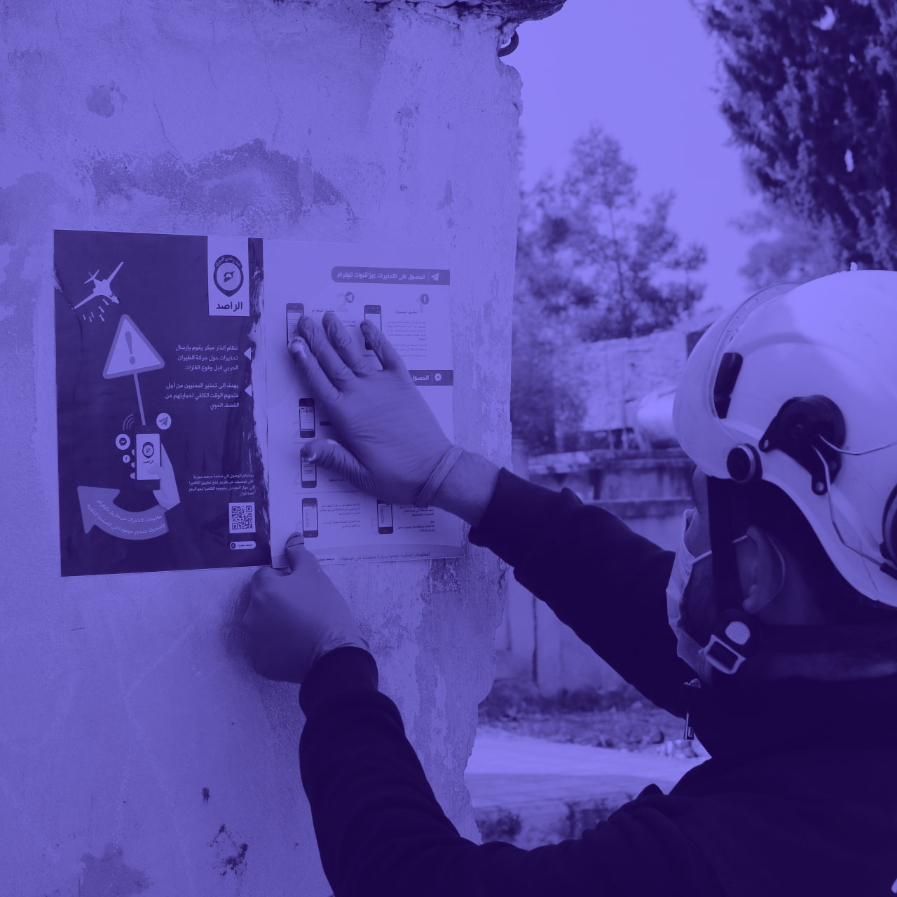 A member of the Syrian Civil Defence putting a poster of Hala's Sentry System up on the wall