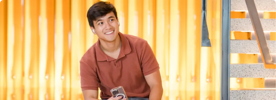 man smiling with headphones in and a smartphone in his hand