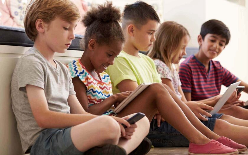 5 Kinder sitzen am Boden und nutzen Ihre Handys und Tablets