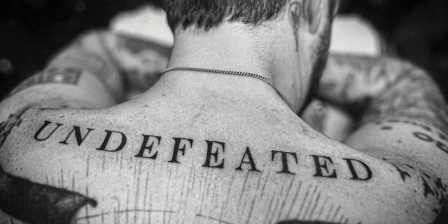 Ein Tattoo: Schriftzug "Undefeated" auf dem Rücken einer Person