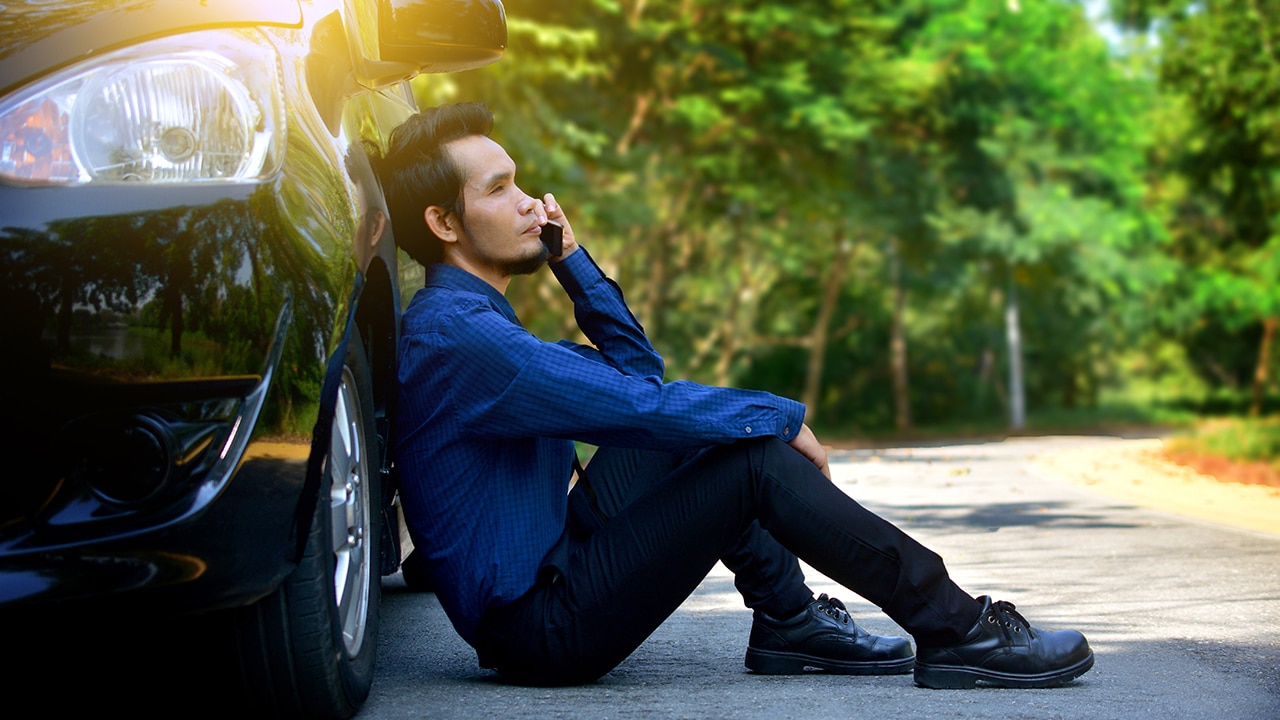 Disappointed man holding smart phone and sitting at car parked on road