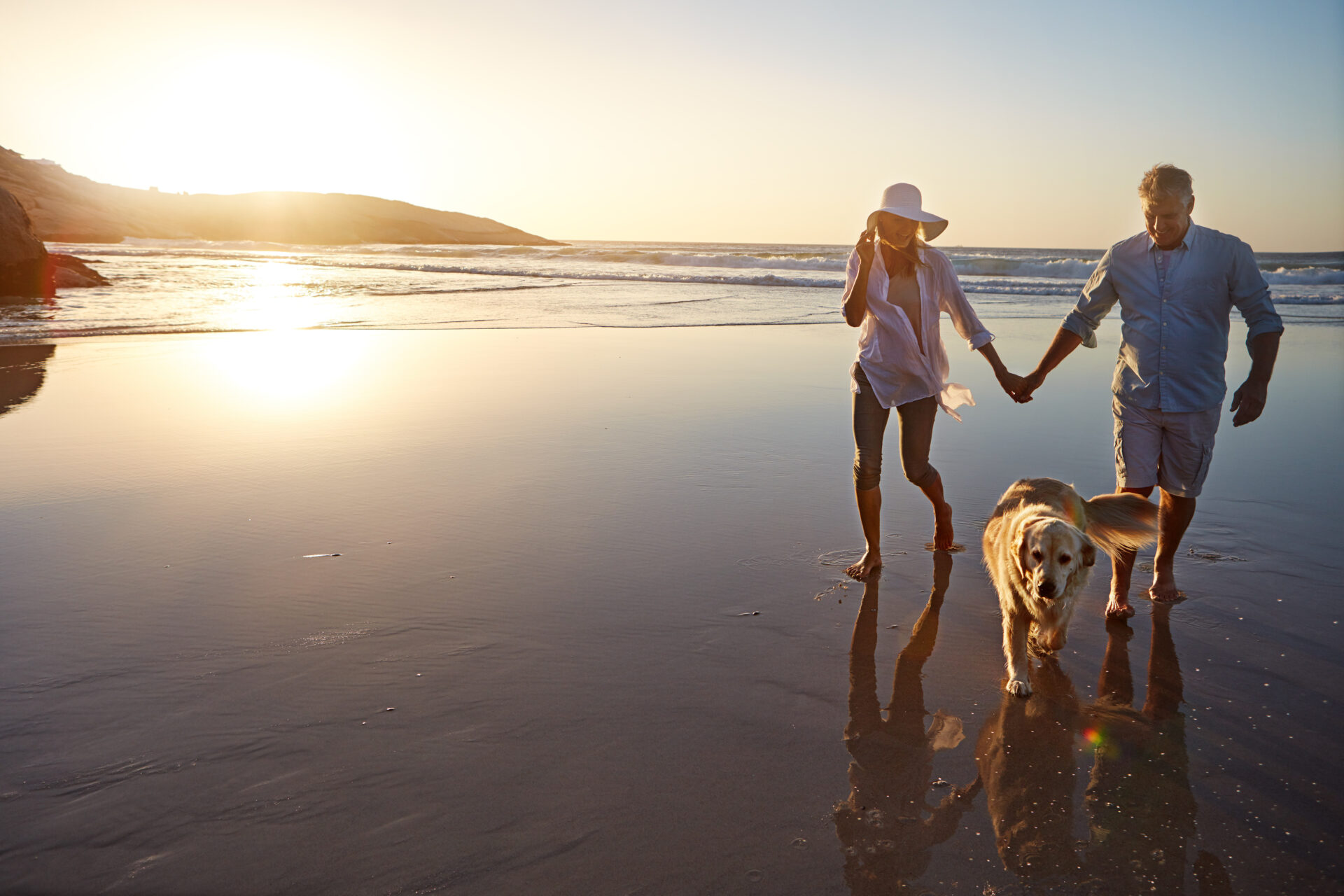 A man and woman stroll along the beach, accompanied by a dog, enjoying a sunny day by the ocean in California.