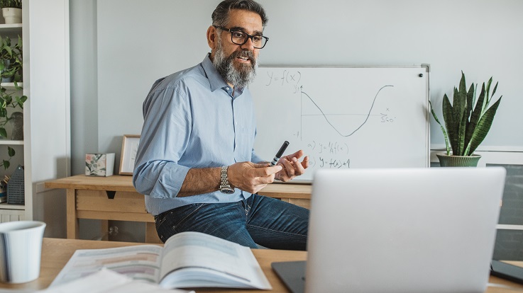 Photo of a teacher at a whiteboard with a laptop.