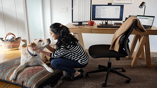 Mujer arrodillada para acariciar a su perro en una oficina doméstica con un escritorio, un ordenador y una silla