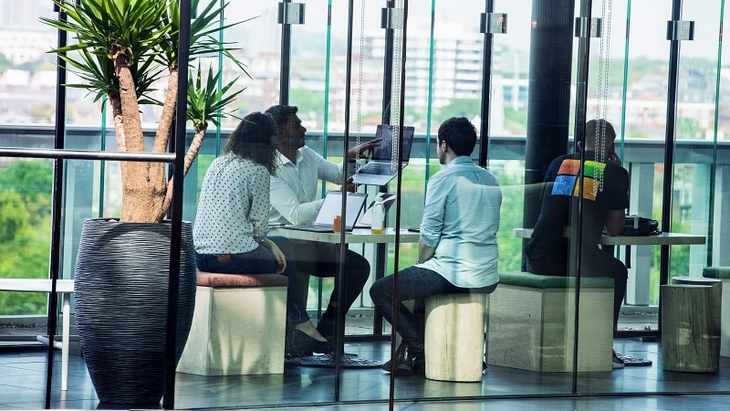 Empat orang berkolaborasi di kantor modern dengan jendela besar dan tampilan kota