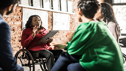 Mulher em cadeira de rodas liderando uma reunião com três colegas em um ambiente de escritório casual