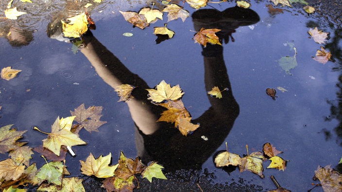 Beine eines Läufers spiegeln sich in einer Pfütze.