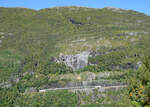 Der ganze 6 Wagen-Zug mit beiden Loks von Flam nach Myrdal in der imposanten Berglandschaft zwischen den Stationen Blomheller und Kjosfossen, fotografiert vom Wanderweg auf der gegenüberliegenden