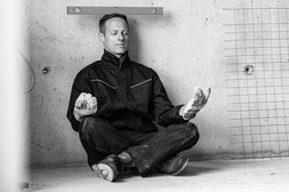 Wissenspodcast: Mid adult worker with level on his head doing Yoga relaxation exercises in Lotus position during a break at construction site. Copy space.