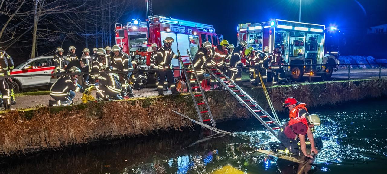 Feuerwehrleute sitzen auf dem Dach eines im Wasser versunkenen Autos und versuchen, die Insassen zu befreien.