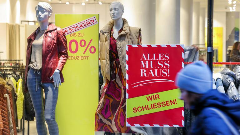 Schaufenster eines Modegeschäftes mit Schildern im Schaufenster, die auf die Schließung der Filiale hinweisen.