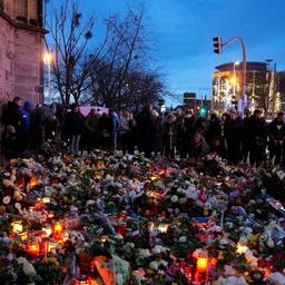 Vor einer Kirche liegen unzählige Blumen, Kerzen und Kränze um die sich Bürger*innen versammelt haben, um zu gedenken.