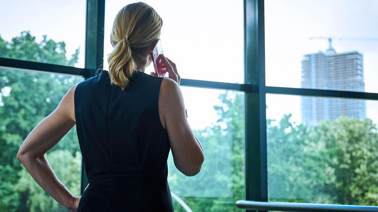 Eine Frau steht in einem Büro am Fenster und telefoniert.