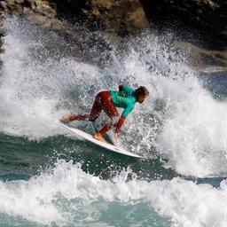 Ein Surfer steht auf seinem Surfbrett umgeben von Wellen an einem Strand.