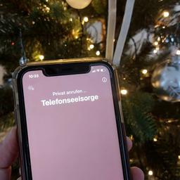 Mit einem Smartphone wird die Nummer der Telefonseelsorge vor einem Weihnachtsbaum gewählt. 