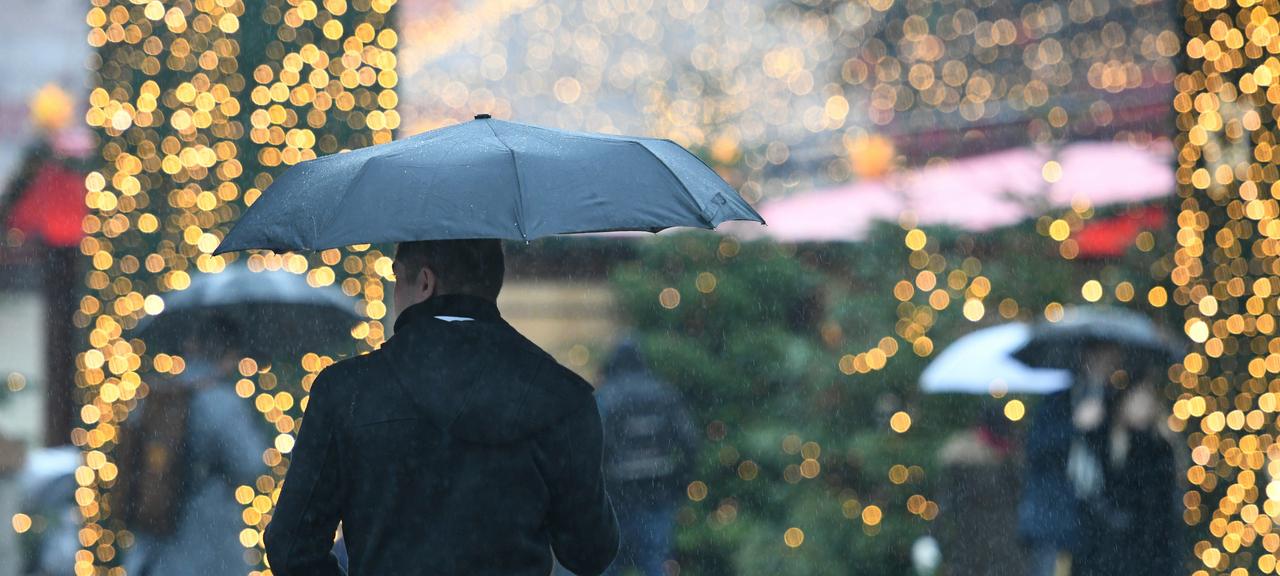 Mann mit Regenschirm läuft an Weihnachtsmarkt entlang