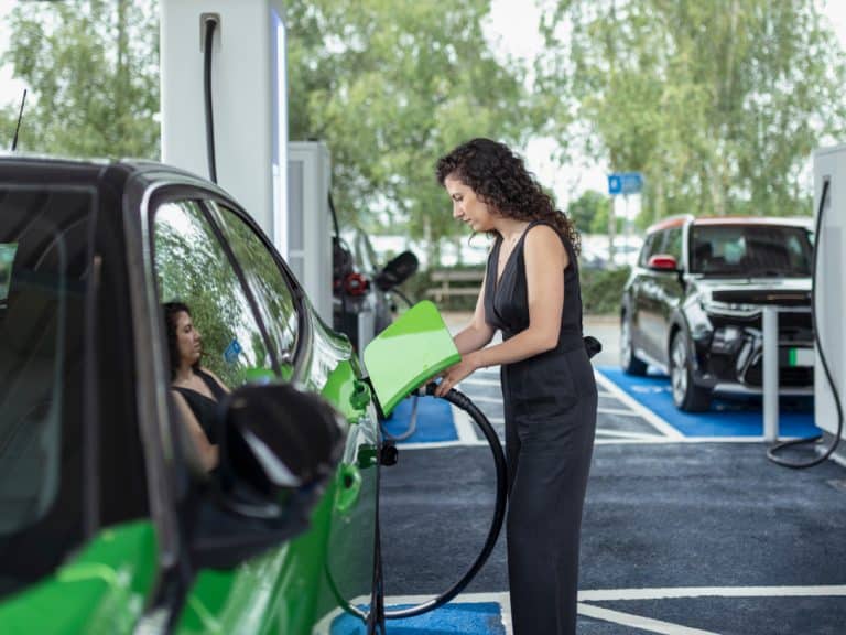 Grünes Auto wird an der Tankstelle von einer Person betankt.