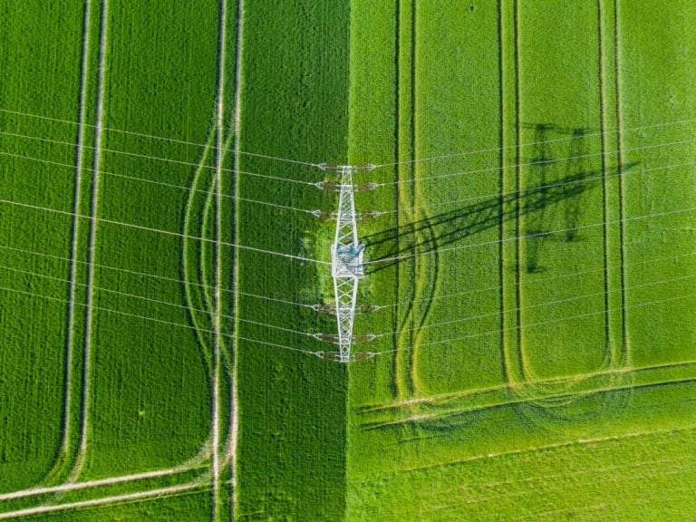 Grünes Feld von oben, mit Schatten von einem Strompfosten.