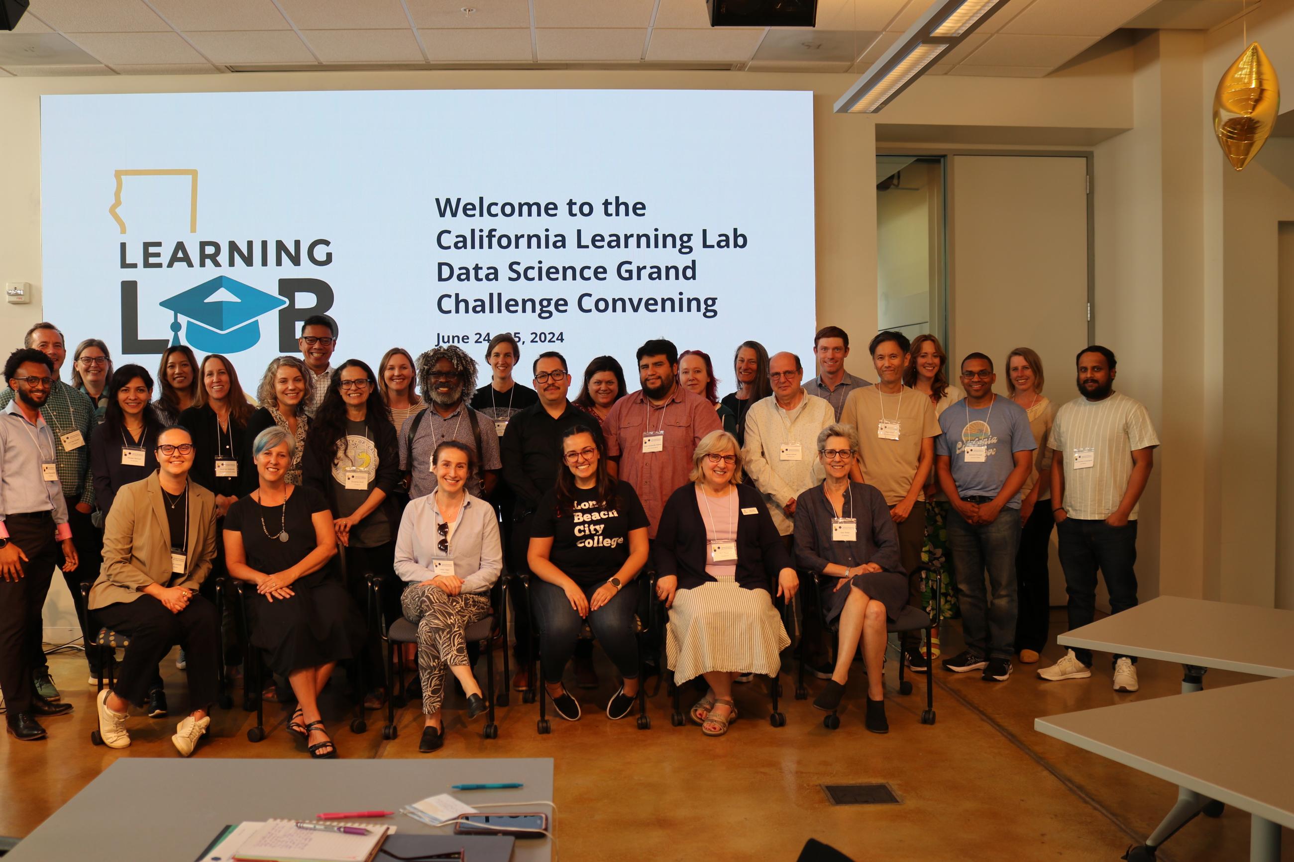 Group of collaborators for california schools pose smile in front of a slide with text, "welcome to the California Learning Lab Data Science Grand Challenge Convening"